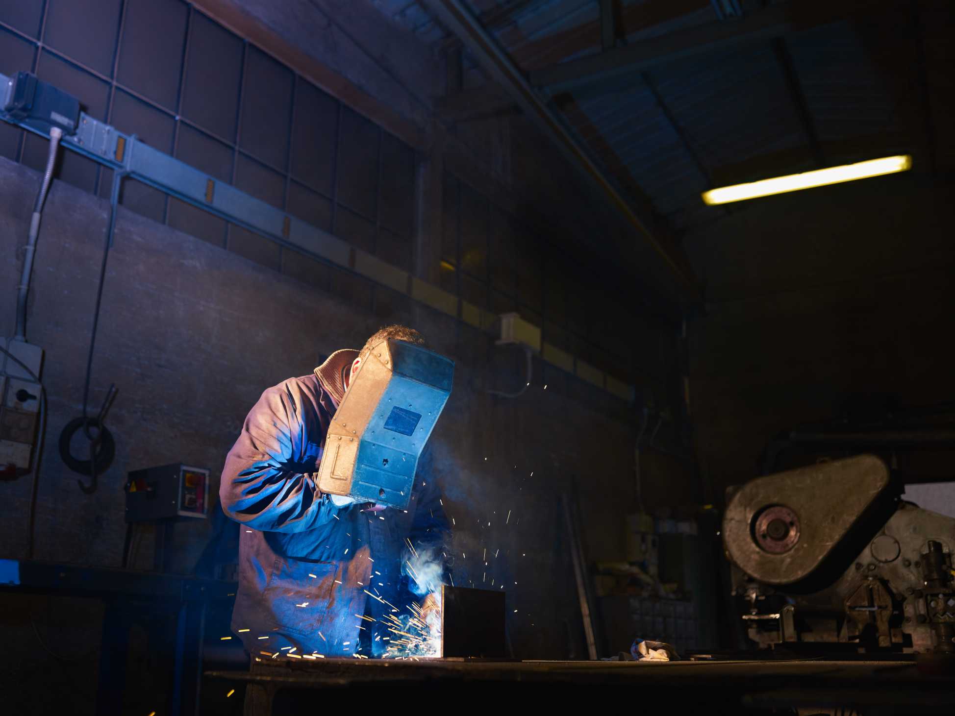Manual worker in steel factory using welding mask, tools and machinery on metal. Horizontal shape, side view, waist up